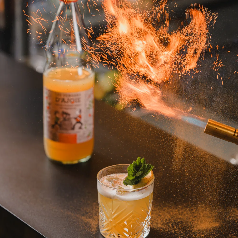 A cocktail being prepared at the bar with a flame and a mint garnish