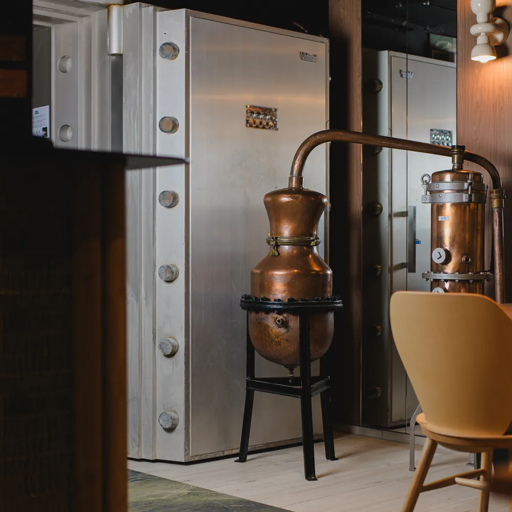 A copper still displayed in front of a vault door inside the restaurant