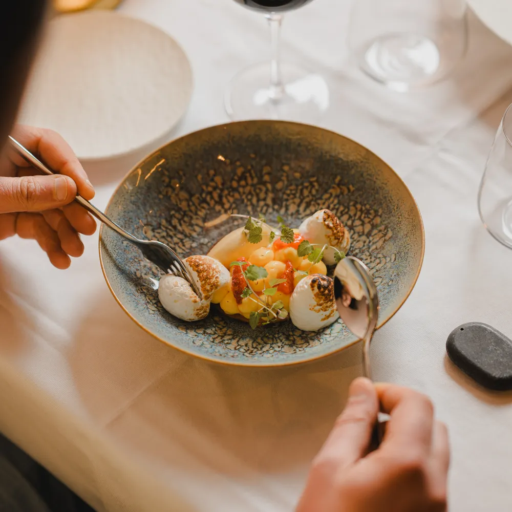 A guest enjoys a colourful dish in a deep plate with a glass of red wine